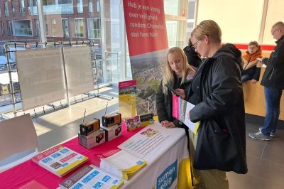 Twee mensen bekijken informatie op een tafel met brochures en promotiemateriaal.