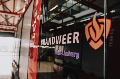 Zijaanzicht van een brandweerwagen met het woord 'BRANDWEER' en een logo.