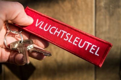 Rode sleutelhanger met het woord "VLUCHTSLEUTEL" en een paar metalen sleutels.